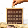 Hand inserting Indian currency note into wooden saving box with denominations grid, cash nearby.