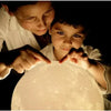 Child and adult touching glowing moon lamp in dark room, soft light, learning together