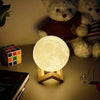 Moon lamp night light on wooden stand with Rubik's cube, notebook, and teddy bears